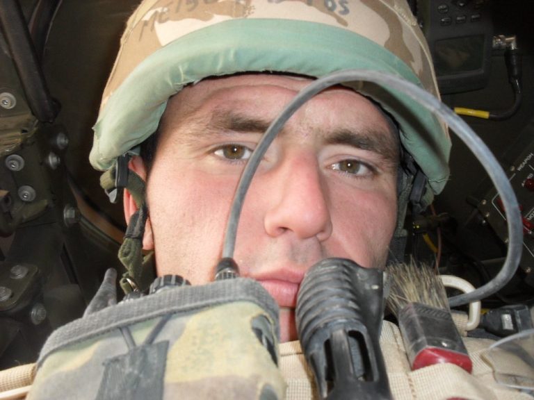 A close-up of a soldier wearing a helmet and military gear in a vehicle.