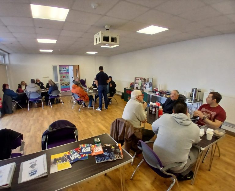 A group of people seated at tables engaged in conversation in a spacious room.